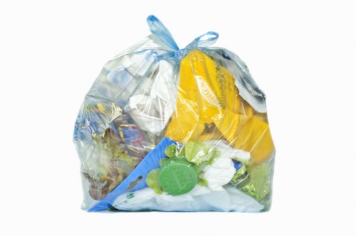 A clear plastic rubbish bag filled with various waste items, including plastic bottles, packaging materials, and miscellaneous refuse, situated on a paved outdoor surface. The bag appears to be tightly closed at the top with a gathered seal, and some of the contents, such as yellow and green plastic objects, are partially visible through the semi-transparent plastic material. It is placed in an outdoor environment, possibly on a driveway or pavement, with no other objects or background details visible. The image is relevant to rubbish removal services offered by Commercial Waste Removal Crouch End, demonstrating typical waste collection and disposal tasks performed by local waste management providers in the Crouch End area. The overall scene emphasizes waste containment and the importance of proper rubbish collection in residential or commercial settings in North London postcode vicinity.
